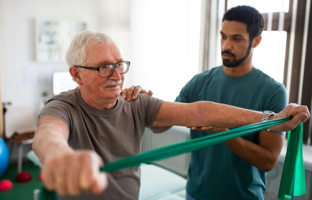 Physio helping senior man work with bands